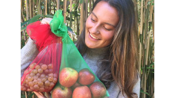 A woman holding two reusable produce bags with fruit in them.