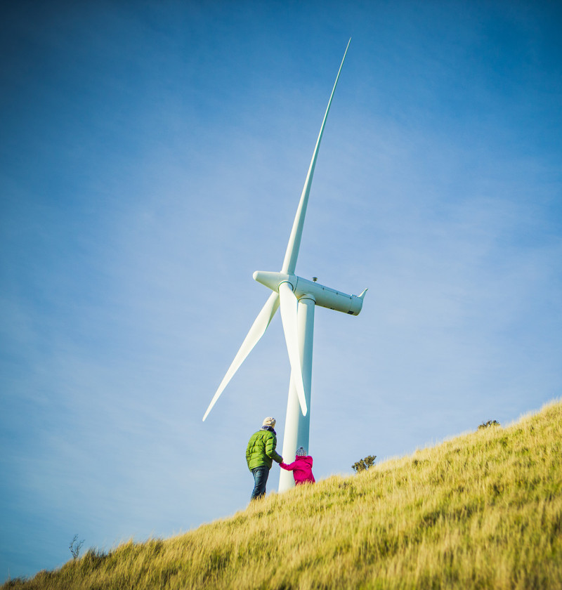 Two people stand by a wind turbine on a hill.
